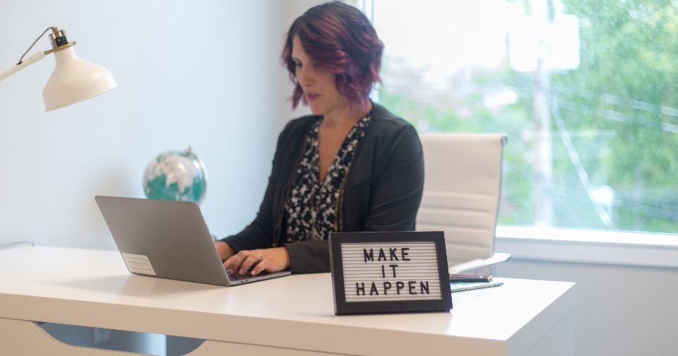 A solo founder working at a home-office desk on a laptop, running her one-person business